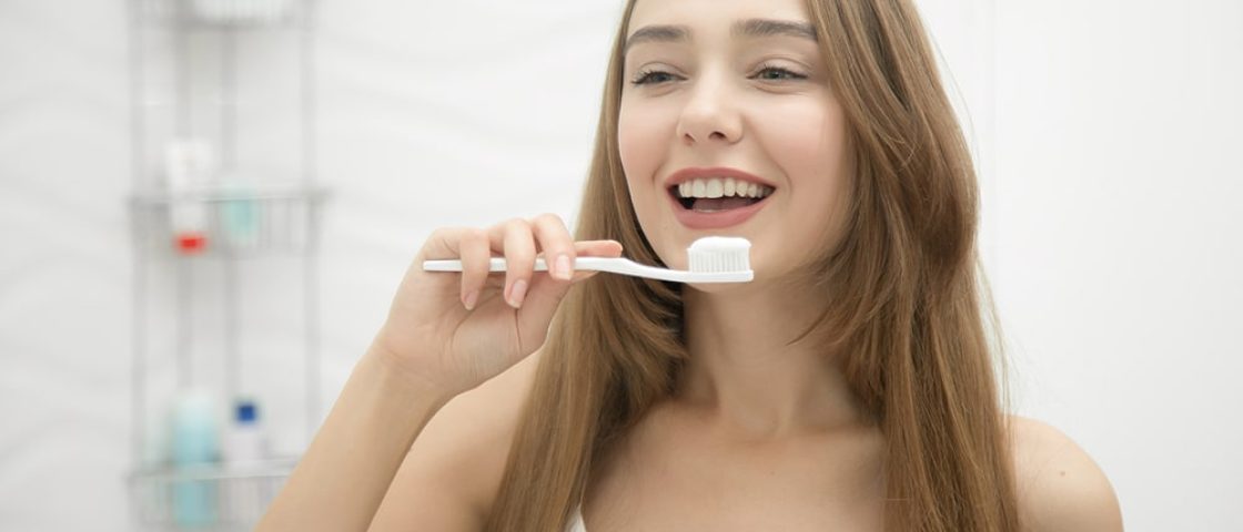 mulher sorrindo segurando escova de dente com creme dental