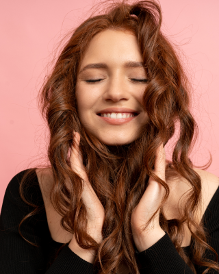 Imagem de uma mulher ruiva sorrindo e encostando as duas mãos nos cabelos, representando novas ideias para pintar o cabelo.
