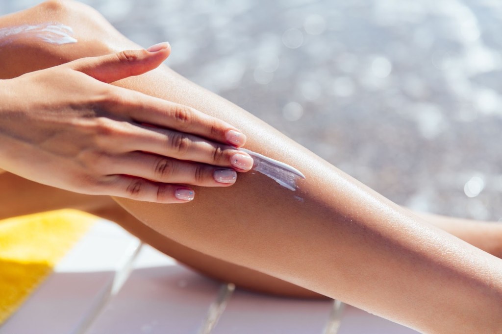 Close-up das pernas de uma pessoa aplicando protetor solar em um dia ensolarado.