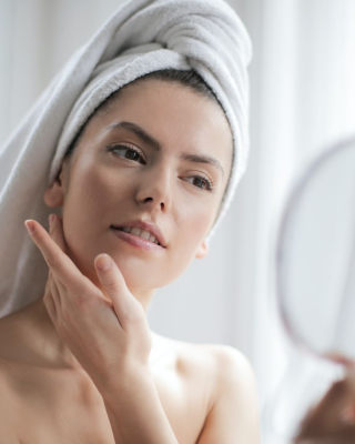 Mulher com toalha enrolada na cabeça olhando reflexo no espelho após adotar a clean beauty.