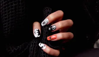 Mão de uma pessoa branca agarrando um tecido preto, com destaque para as unhas decoradas de Halloween.