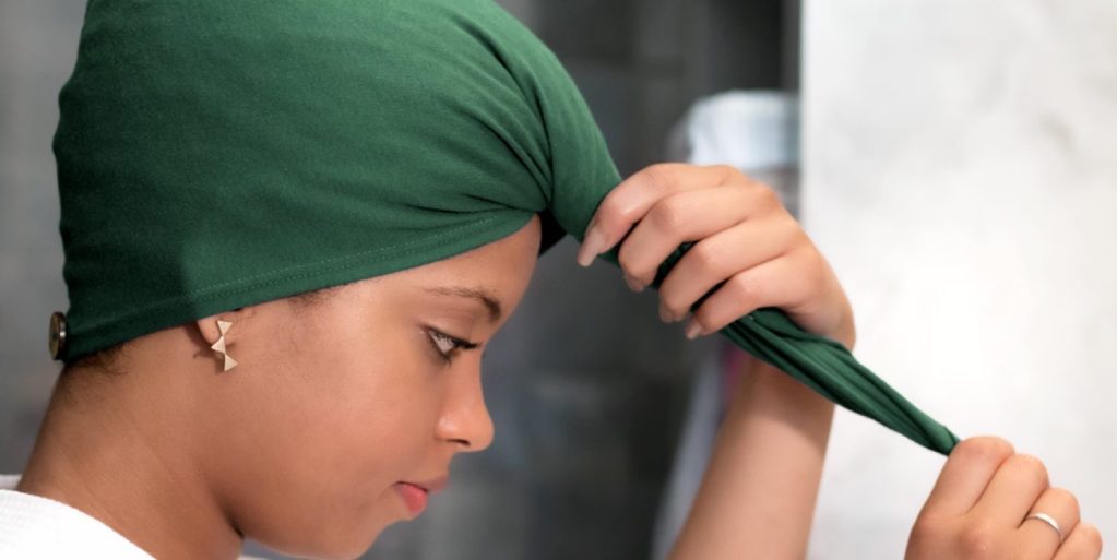 Mulher amarrando uma toalha verde na cabeça estilo turbante para ilustrar o plopping.