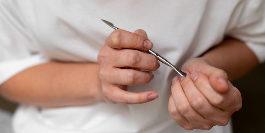 Close-up de uma mulher tendo cuidados com as mãos ao arrastar cutículas gentilmente com um instrumento de cutilagem.