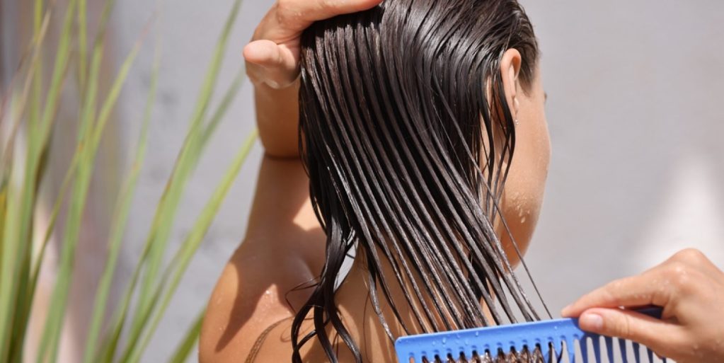 Close-up visto de trás de mulher que sabe como tirar frizz do cabelo ao pentear os fios com creme de tratamento hidratante.
