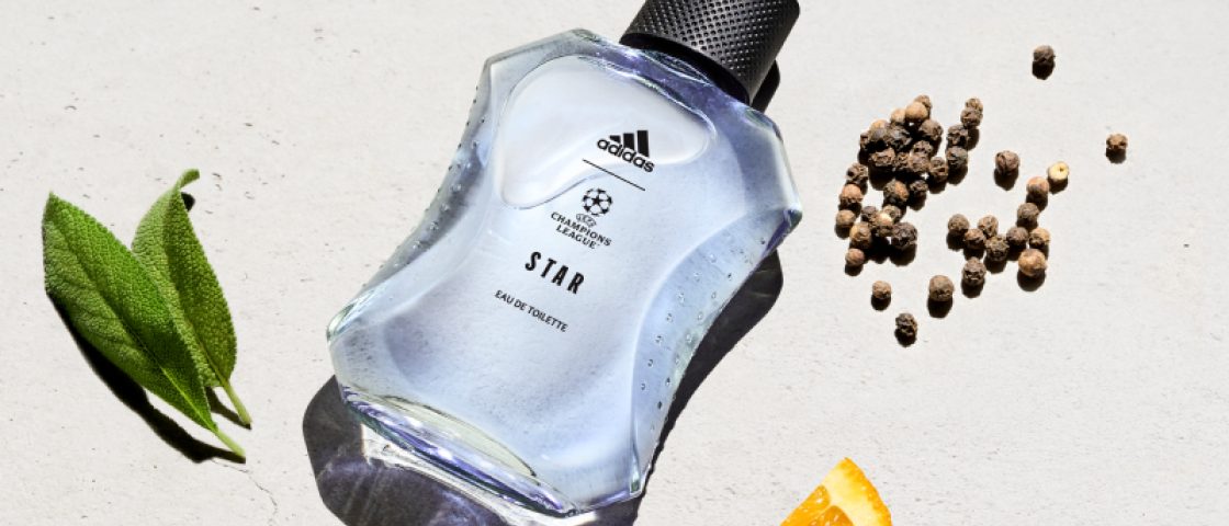 Frasco do perfume Adidas UEFA Star deitado em um fundo branco com elementos que representam suas notas olfativas, como uma fatia de tangerina.